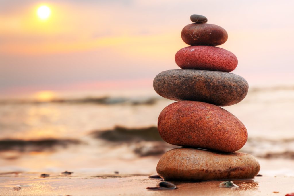 Ein Stapel Steine am Strand bei Sonnenuntergang als Symbol für das Gleichgewicht der Hormone
