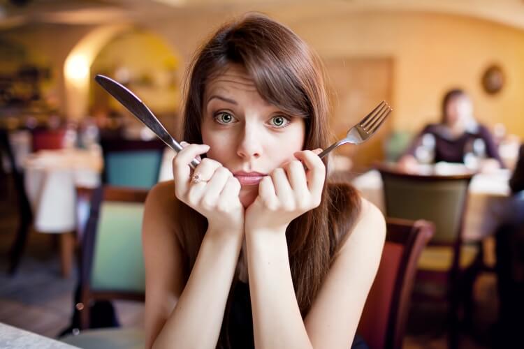 unvertraeglichkeiten: Frau mit Besteck in den Händen, die ratlos schaut und nicht weiß, was sie essen soll